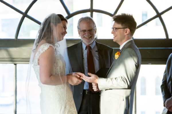 Bride and groom exchanging rings during a wedding ceremony at Windows on the River Bridgeview Room in Cleveland, Ohio