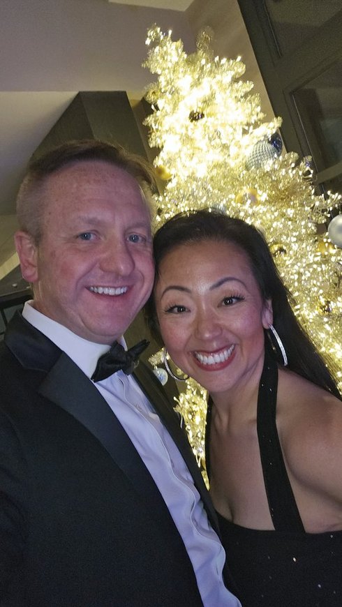A smiling couple, Paul and Lana, in formal evening wear posing in front of a glowing white Christmas tree at a 2025 New Year's Eve party