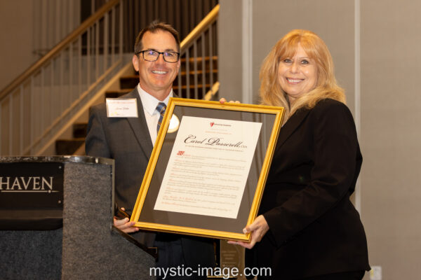 Jason Potter and Carol Passerell smile, holding a framed University Hospitals resolution appointing Carol Passerell, CVA.